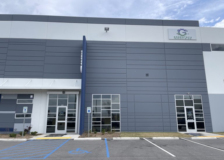 Direct front view of Greentech Renewables building. The building is grey with blue and white accents. There are large "CED" letters on the ledge and a full color logo with "Greentech Renewables" on the front and doors.