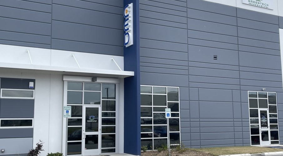 Side angled front view of Greentech Renewables building. The building is grey with blue and white accents. There are large "CED" letters on the ledge and a full color logo with "Greentech Renewables" on the front and doors.